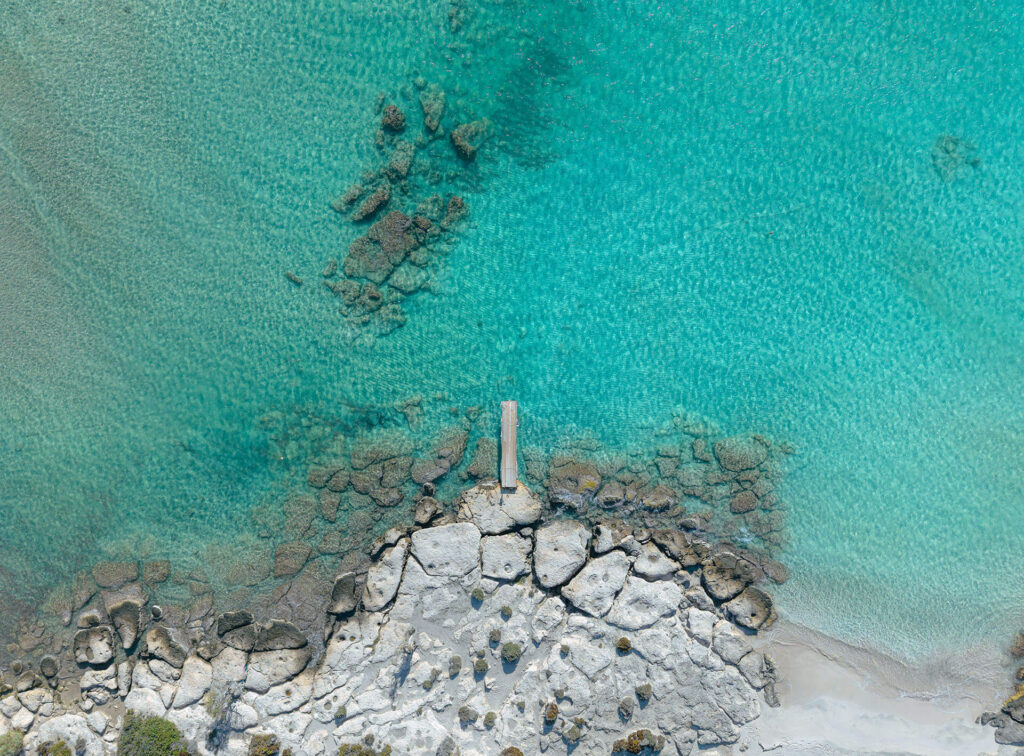 Aerial image of shallow clear water near Elafonisi with rocks and turquoise tones.