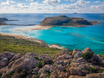 A serene aerial perspective of Balos Lagoon, where turquoise waters fade into pale sand and open sea. Aerial view of Balos Lagoon in Crete with turquoise water, pale sandbanks, and the Mediterranean Sea beyond.
