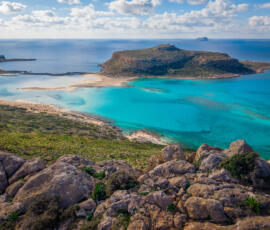 A serene aerial perspective of Balos Lagoon, where turquoise waters fade into pale sand and open sea. Aerial view of Balos Lagoon in Crete with turquoise water, pale sandbanks, and the Mediterranean Sea beyond.