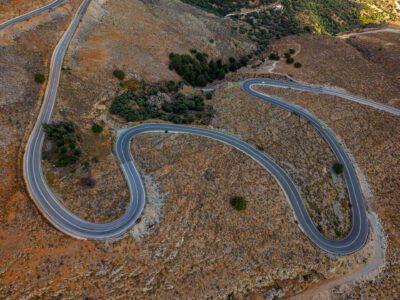 Curving mountain road flowing through golden Cretan hills. Aerial view of a winding mountain road in the hills of Crete.