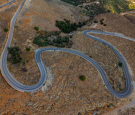 Curving mountain road flowing through golden Cretan hills. Aerial view of a winding mountain road in the hills of Crete.