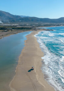 Gentle waves flowing across the shoreline at Falassarna Beach, capturing the movement of the Cretan coast. Shallow waves washing over the sand at Falassarna Beach in western Crete, viewed from above.