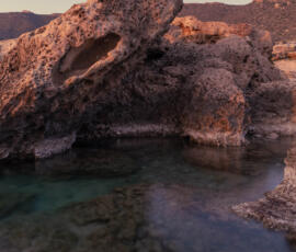 A crystal-clear rock pool hidden beneath sculpted volcanic formations along the Falassarna coast. Clear natural rock pool beneath volcanic rock formations on the Falassarna coast in Crete.
