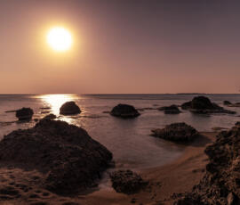 Golden sunset light reflecting across calm water and volcanic rocks along the Falassarna coastline. Sunset over volcanic rocks and calm sea at Falassarna beach in Crete.