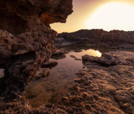 A quiet tidal pool glowing in the last golden light of sunset along the rocky coast of Falassarna. Sunset tidal pool among volcanic rocks on the Falassarna coast in Crete.