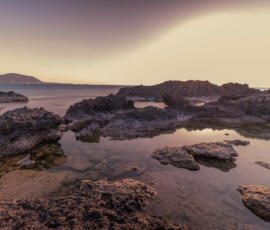 Still tidal pools reflecting the warm evening light along the rocky coast of Falassarna. Natural tidal pools in volcanic rocks at Falassarna coast during golden hour in Crete.